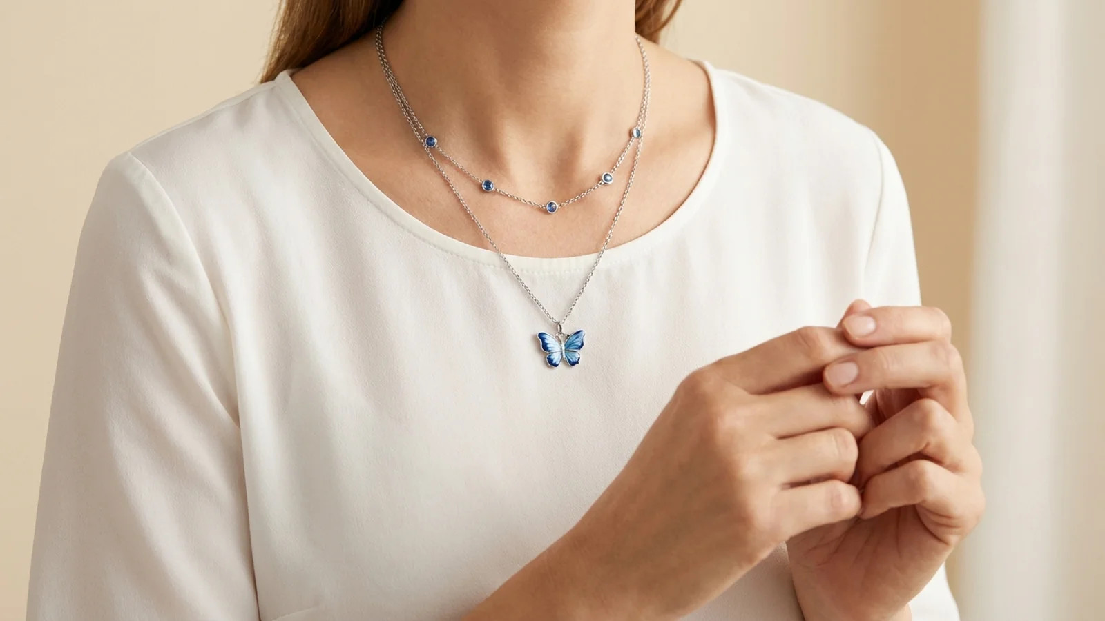 Blue butterfly pendant layered with a shorter blue-accent chain over a white blouse