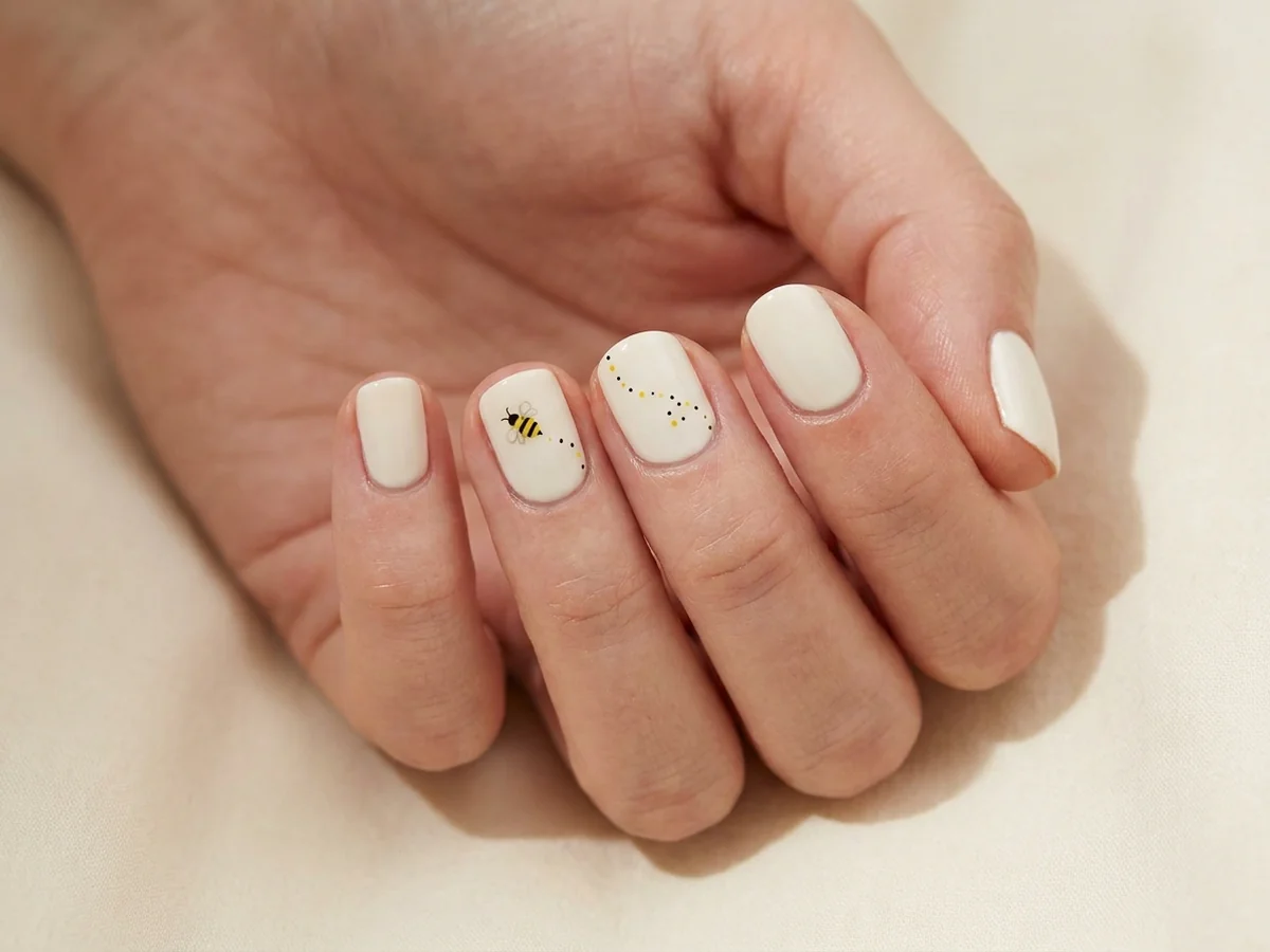 Cream nails with a simple bee accent and dotted flight trail